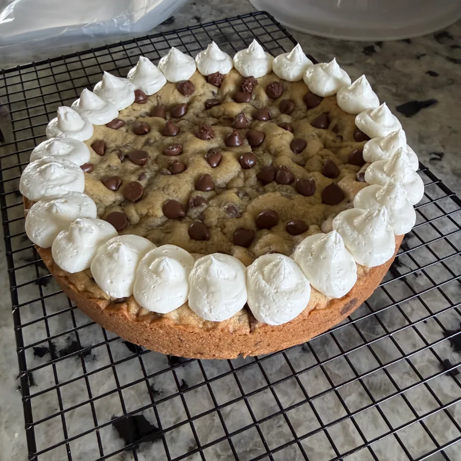 A round double-layer chocolate chip cookie cake edged with piped buttercream rosettes