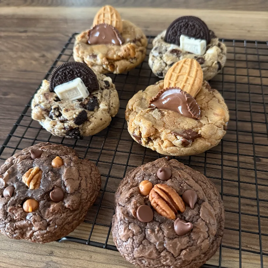 Six thick gourmet cookies on a cooling rack, stuffed with peanut butter cups, Oreos and Biscoff